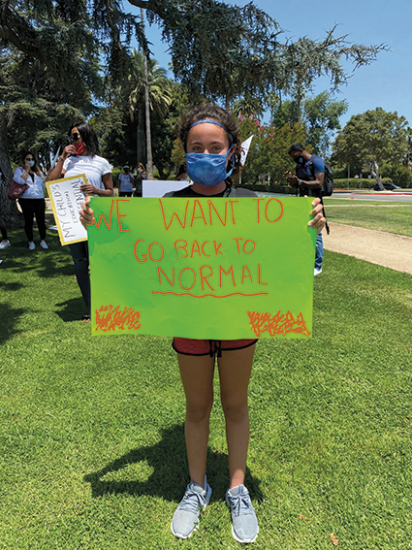 young woman holding homemade sign reading "I want to go back to normal"