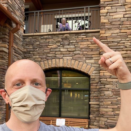 john in mask pointing at second story balcony where mom sits